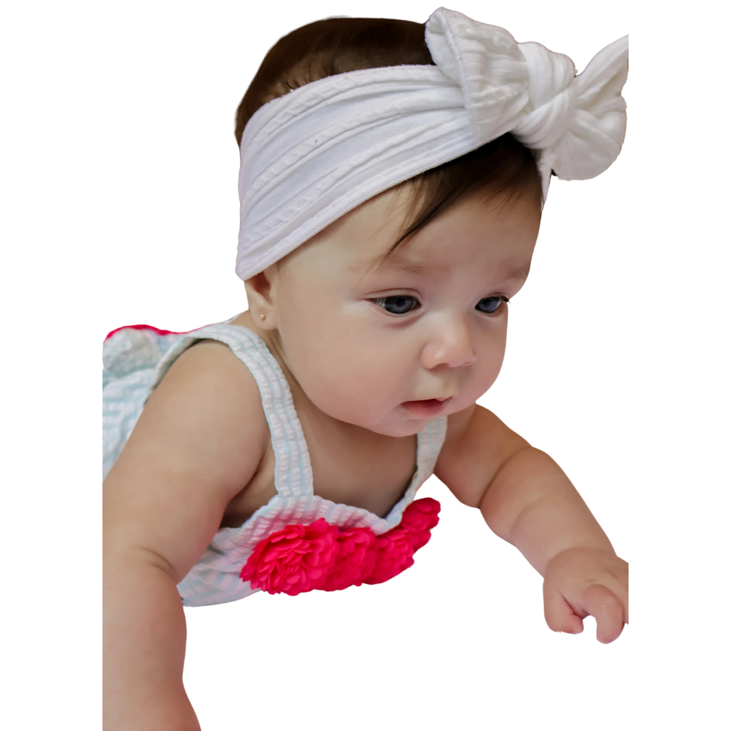 Baby girl with newly pierced ears wearing a pink polka-dot shirt, looking up with pink flower illustrations in the background. Safe infant ear piercing at Peekaboo Piercing in Tampa