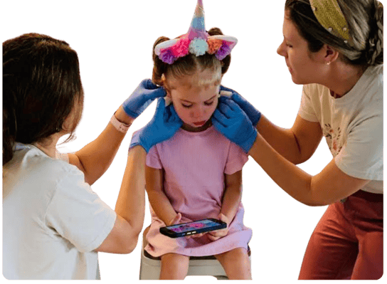 Young girl with a unicorn headband getting both ears pierced at the same time by two professionals wearing gloves, with flower illustrations in the background. Simultaneous ear piercing service at Peekaboo Piercing in Tampa.