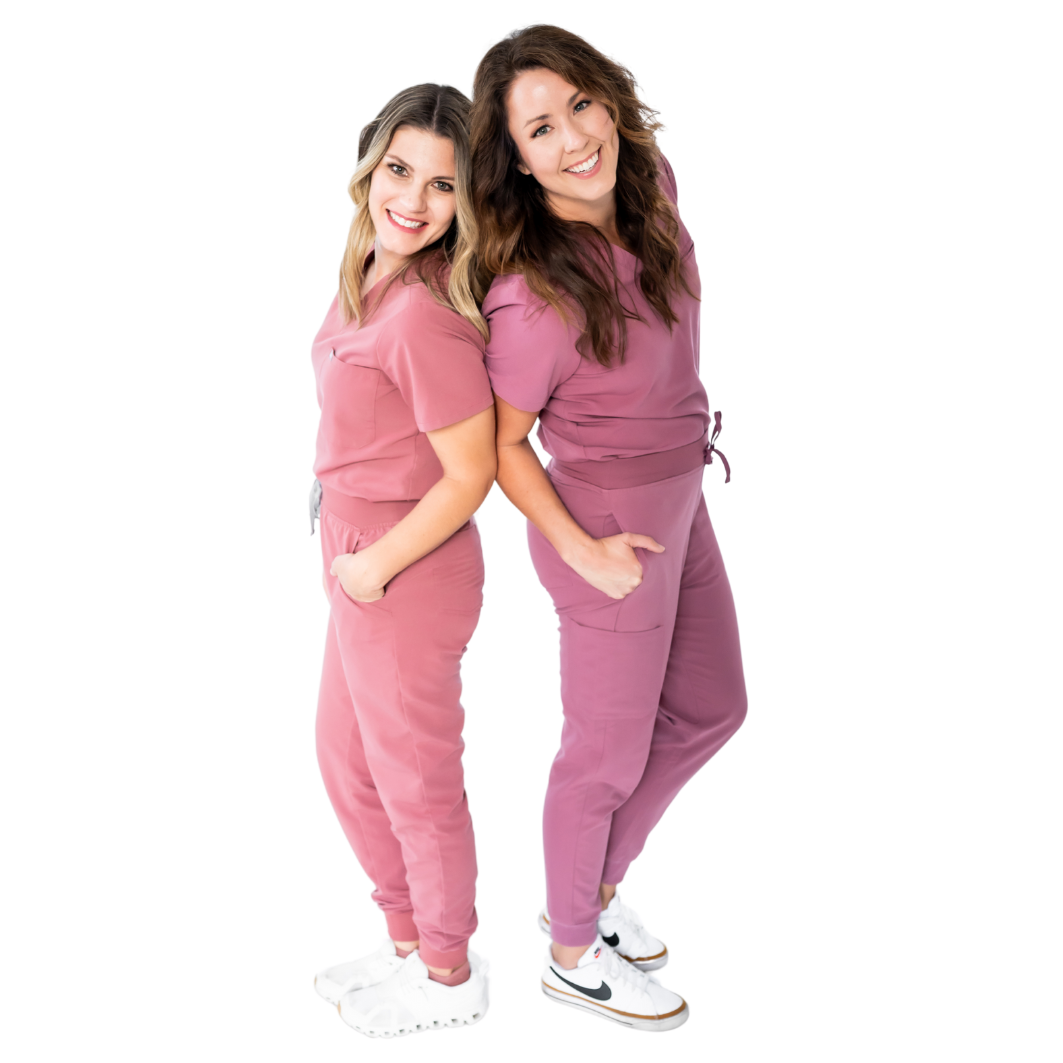 Two smiling women in pink and mauve scrubs standing back to back with hands in their pockets, surrounded by flower graphics. The friendly team behind Peekaboo Piercing in Tampa, specializing in safe medical ear piercing.